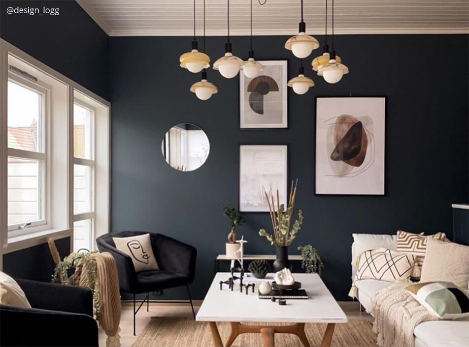 Obývací pokoj s tmavými stěnami, černá sametová křesla, kulaté zrcadlo, grafické plakáty